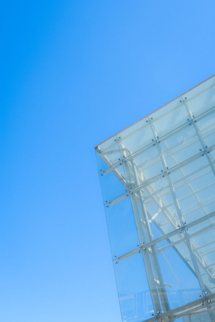 Low angle view of a modern glass building facade under a clear blue sky, showcasing architectural innovation.