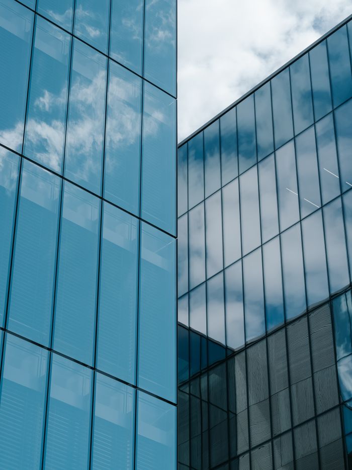 A low-angle shot of a contemporary glass skyscraper reflecting the sky and clouds.