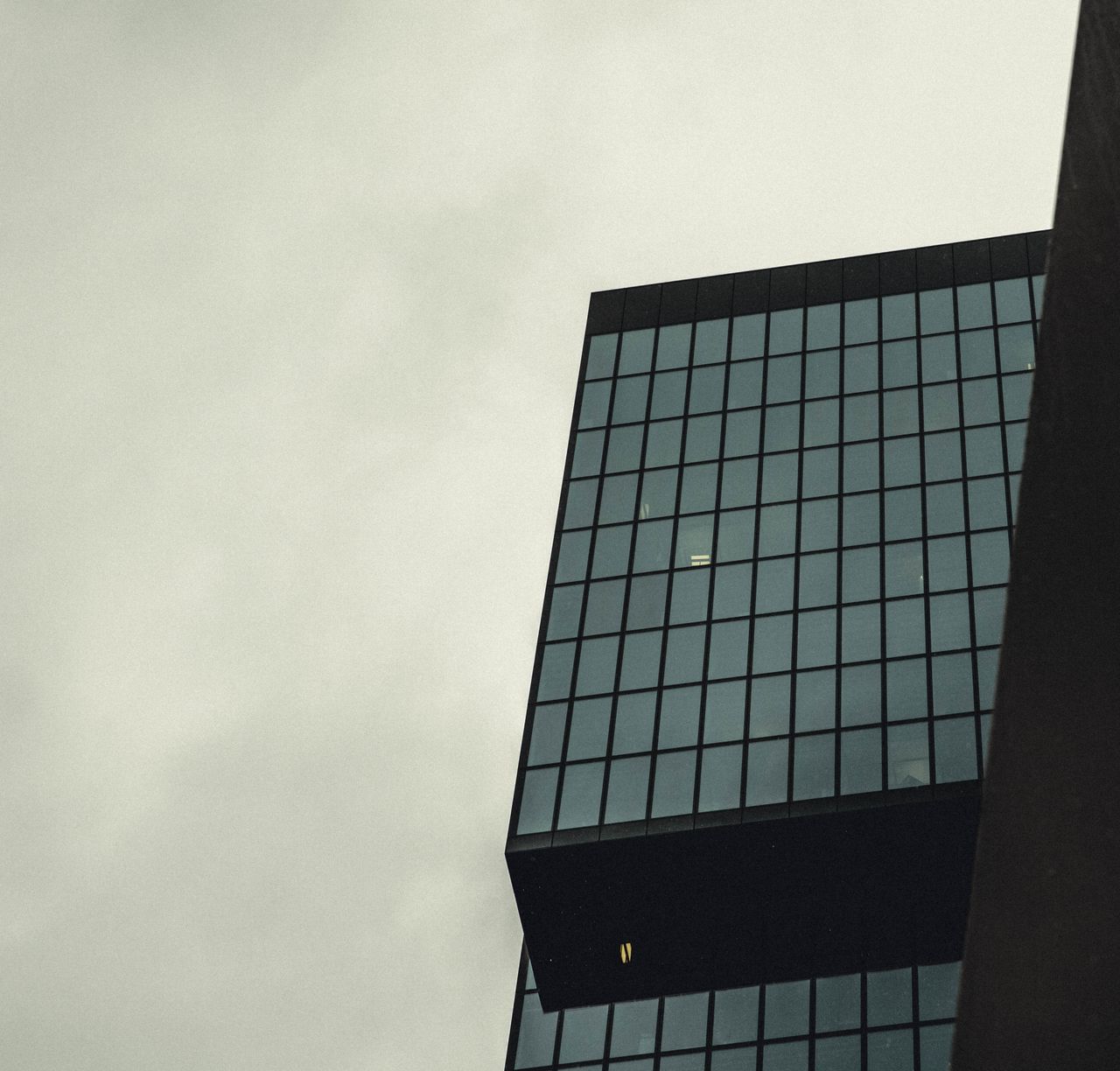 Low angle view of a modern skyscraper with a glass facade against a cloudy sky.