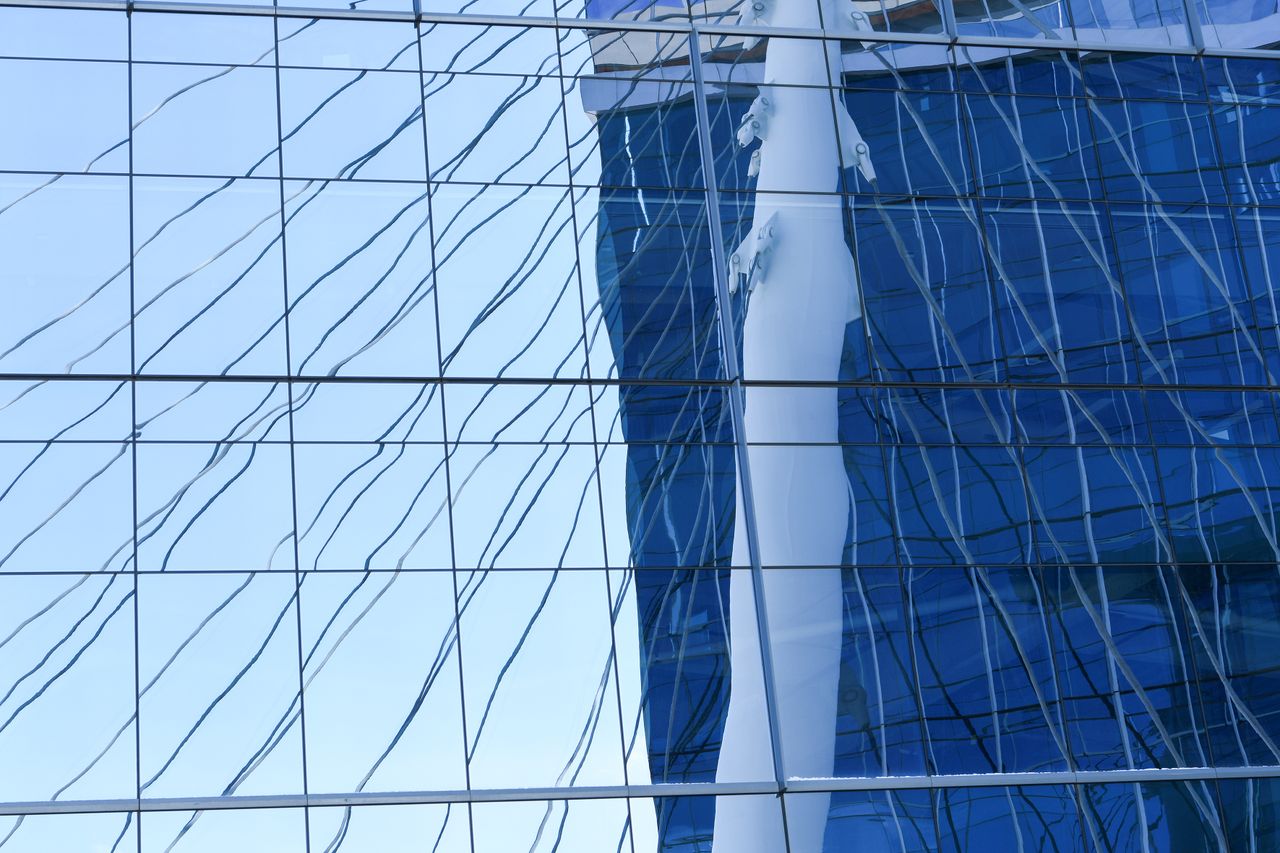 Reflection of a modern building facade captured in glass panels, showing abstract lines.